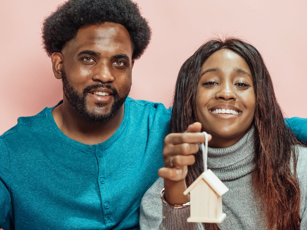 Smiling couple holding a house ornament, symbolizing home ownership and happiness.